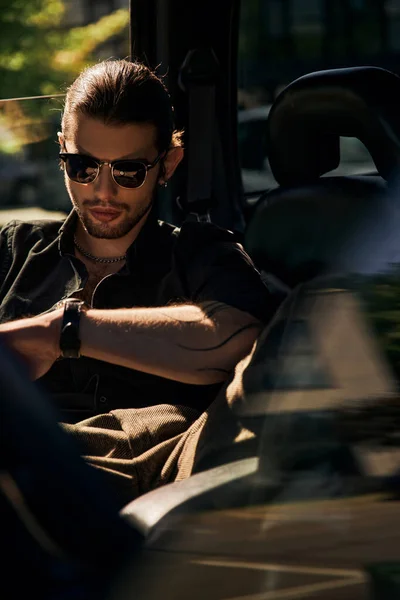 Tiro vertical de buen aspecto atractivo hombre con tatuaje relajante en el asiento trasero de su coche, conductor sexy - foto de stock