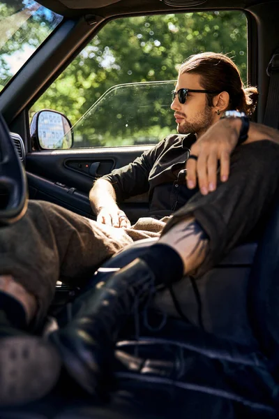 Handsome eye catching male model in elegant black outfit with accessories relaxing in his car — Stock Photo