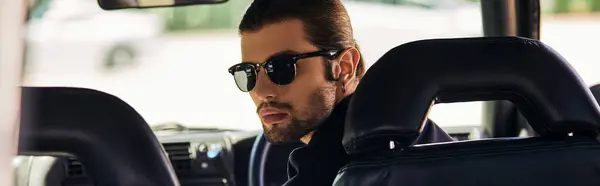 Good looking man in black outfit behind steering wheel and looking at camera, sexy driver, banner — Stock Photo