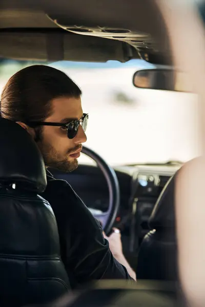 Tiro vertical de boa aparência modelo masculino em preto elegante traje no volante, girando a cabeça — Fotografia de Stock