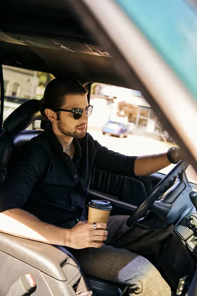 Conducteur tentant avec boucle d'oreille et montre-bracelet tenant tasse de café tout en étant assis derrière le volant — Photo de stock
