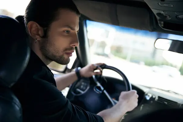 Sexy hombre elegante con pendiente y reloj de pulsera en traje negro que conduce su coche, concepto de moda - foto de stock