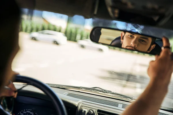 Appealing young man behind steering wheel of his car and looking in rearview mirror, sexy driver — Stock Photo