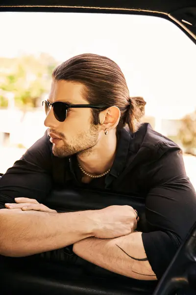 Appealing sexy man with accessories in stylish black attire posing near his car and looking way — Stock Photo