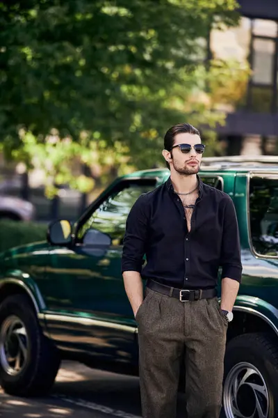 Vertical shot of charming man in elegant black attire posing next to car with hands in pockets — Stock Photo