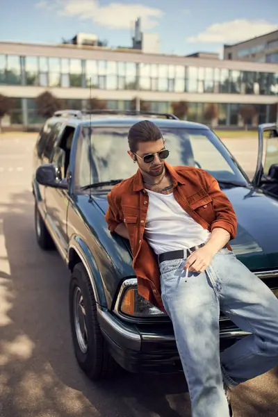 Hombre sexy de buen aspecto en traje brillante de moda posando junto a su coche con el cigarrillo en la mano - foto de stock