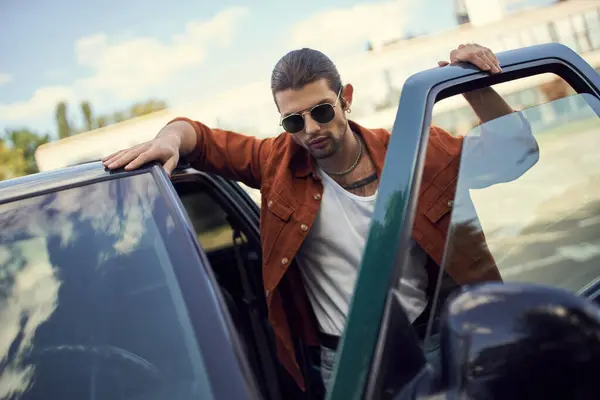 Schöner sexy Mann mit Sonnenbrille und Pferdeschwanz in lebendigem Outfit posiert neben seinem Auto — Stockfoto