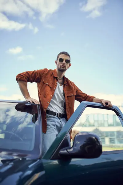 Vertical shot of appealing young man in stylish vibrant clothing posing next to his car, fashion — Stock Photo