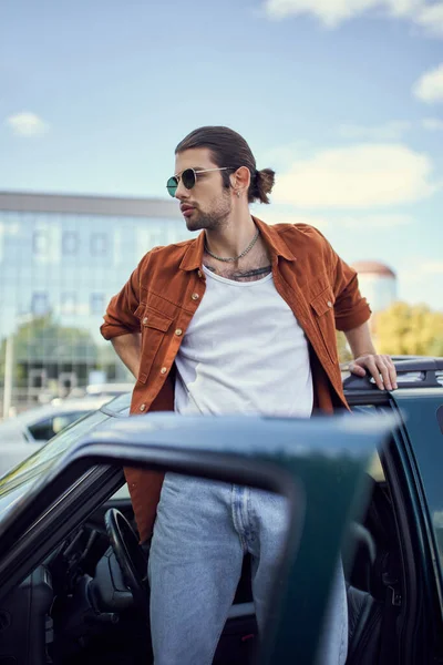 Junge charmante männliche Modell posiert in lebendiger Kleidung neben seinem Auto mit geöffneter Tür, Stil-Konzept — Stockfoto