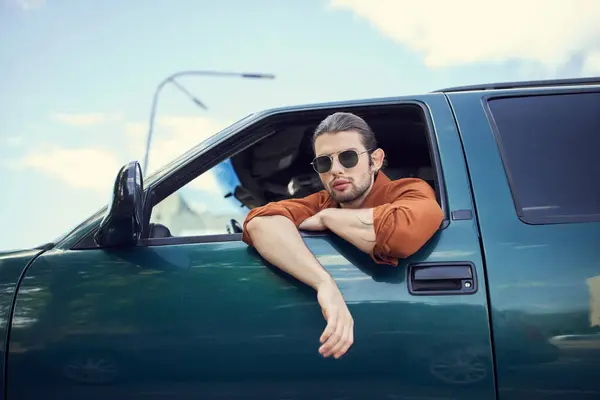 Handsome young male model with sunglasses looking through car window at camera, fashion and style — Stock Photo