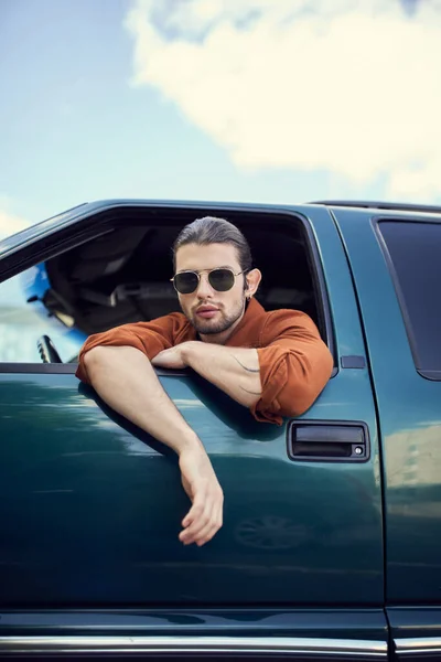 Charming young man in brown shirt with sunglasses looking through car window, style and fashion — Stock Photo