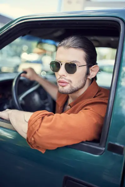 Attraktiver junger Mann mit Ohrring im trendigen braunen Hemd mit Sonnenbrille schaut aus dem Autofenster — Stockfoto