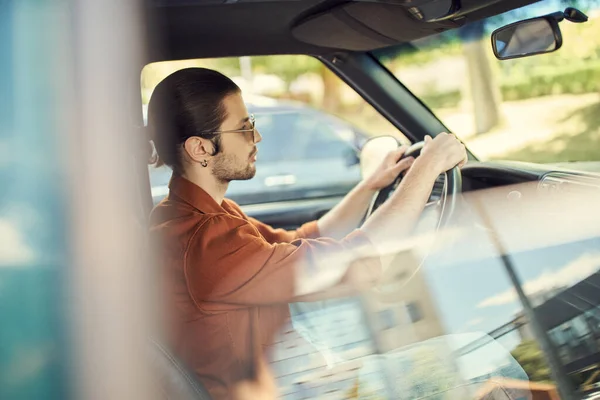 Gut aussehender sexy Mann in braunem Hemd mit Sonnenbrille und Ohrring am Steuer seines Autos, Mode und Stil — Stockfoto