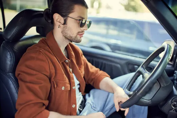 Attraktiver junger Mann in stylischem, lebendigem Outfit posiert im Profil im Auto am Steuer — Stockfoto