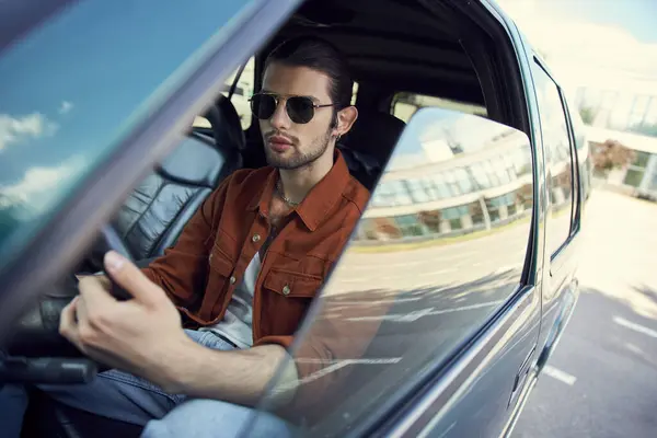 Bel giovane modello maschile in elegante camicia marrone con occhiali da sole al volante, pilota sexy — Foto stock