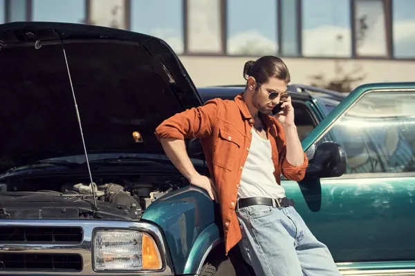 Хороший водій з сонцезахисними окулярами в коричневій сорочці, що стоїть поруч зі своєю машиною, називає свого страховика — стокове фото