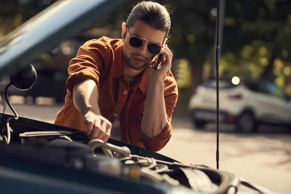 Молодий чоловік у стильному вбранні кличе свого страховика і дивиться на відкриту витяжку свого автомобіля — стокове фото