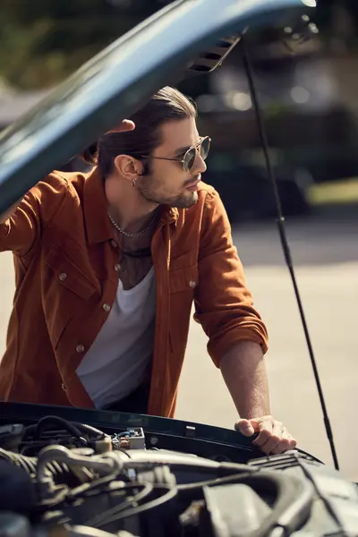 Good looking male model with sunglasses standing next to opened engine hood and looking away — Stock Photo