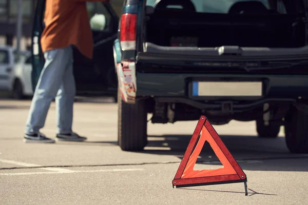 Vista recortada de un hombre joven y elegante de pie junto a su coche con triángulo de advertencia, foto borrosa - foto de stock