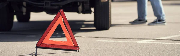 Обрезанный вид на предупреждающий треугольник перед молодым мужчиной-моделью, стоящим возле его машины, баннер — стоковое фото