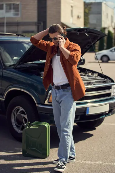 Hombre guapo con gafas de sol y cola de caballo hablando por teléfono con su aseguradora, bote de gasolina - foto de stock