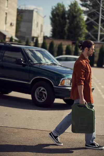 Beau chauffeur sexy en chemise marron et jeans marchant avec une cartouche d'essence dans ses mains — Photo de stock