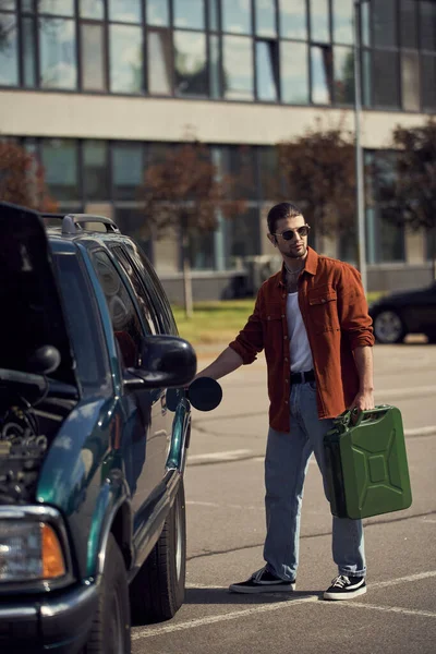 Beau modèle masculin sexy en chemise marron et jeans avec des lunettes de soleil élégantes ravitailler sa voiture — Photo de stock