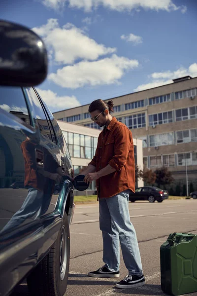 Vertical shot of attractive male model in stylish brown shirt refueling his car with petrol — Stock Photo