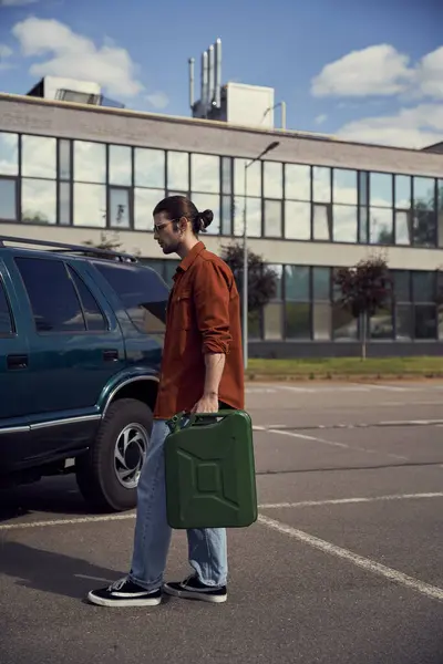 Красивий молодий чоловік в коричневій сорочці з джинсами з бензиновою каністрою в руці йде до своєї машини — стокове фото