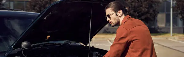 Homem de boa aparência com óculos de sol elegantes em pé ao lado de seu carro com capuz de motor aberto, banner — Fotografia de Stock