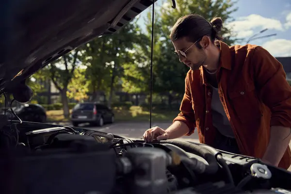 Pensive handsome man in stylish outfit with sunglasses and ponytail checking on his car engine — Stock Photo