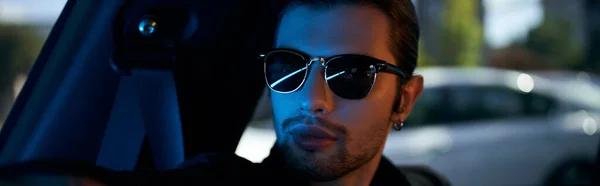 Спокусливий молодий чоловік в елегантному чорному одязі з сонцезахисними окулярами, сидячи в його машині, сексуальний водій, банер — стокове фото