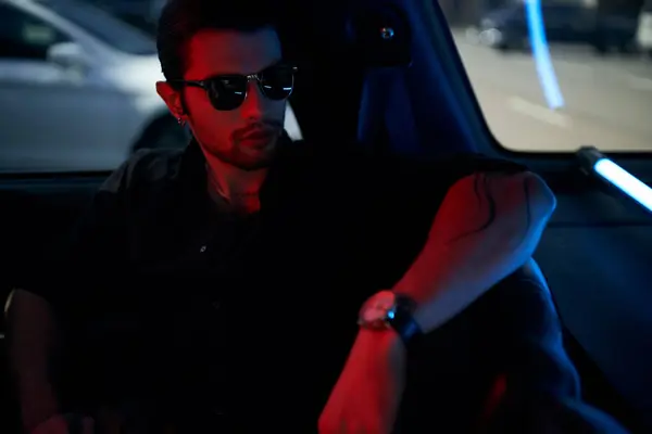 Handsome sexy driver in black shirt with sunglasses and tattoo posing in his car, fashion concept — Stock Photo