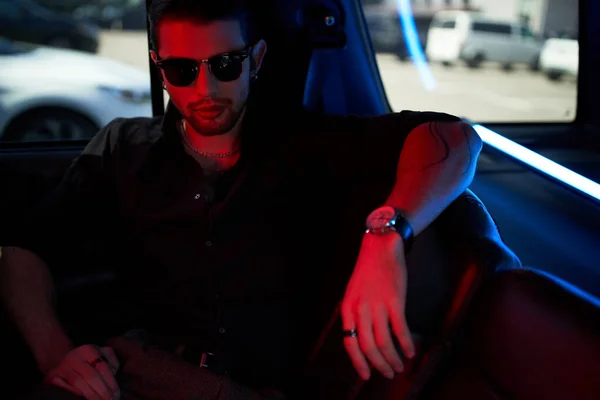 Красивый мужчина в стильной черной рубашке с солнцезащитными очками, смотрящий на камеру, сидящую в его машине — стоковое фото
