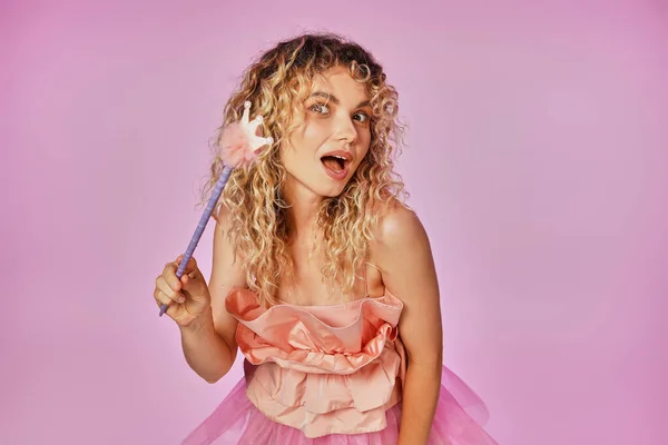 Кудрявая блондинка в розовом наряде зубной феи держит волшебную палочку и смотрит в камеру — стоковое фото