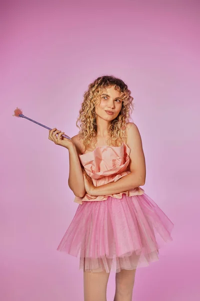 Fröhliche hübsche Frau im rosafarbenen Outfit der Zahnfee mit Zauberstab und leicht verschränkten Armen — Stockfoto
