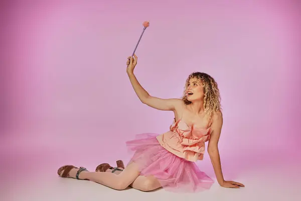 Веселая блондинка с вьющимися волосами, позирующая на розовом фоне в костюме зубной феи с волшебной палочкой — стоковое фото