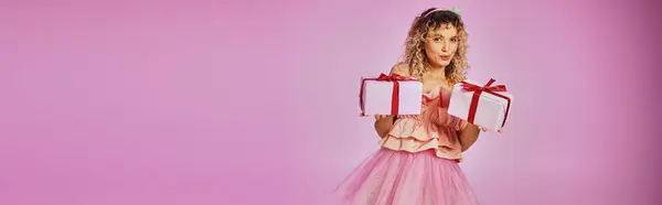 Belle femme blonde en costume de fée dentaire montrant des cadeaux sur la caméra sur fond rose, bannière — Photo de stock