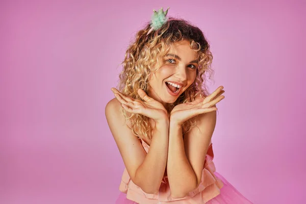 Cheerful attractive woman in pink costume of tooth fairy smiling at camera with hands close to face — Stock Photo