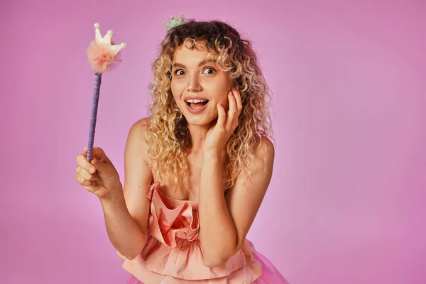 Amazed jolly blonde woman in pink costume of tooth fairy holding magic wand and looking at camera — Stock Photo