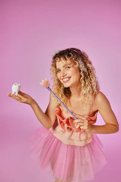Грайлива красива блондинка в рожевому костюмі фея посміхається і заклинання на дитячому зубі — стокове фото