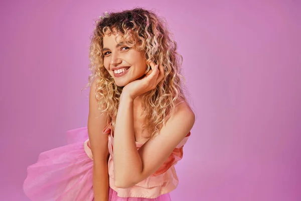 Close up of joyous lovely woman in pink outfit smiling sincerely at camera with hand raised to face — Stock Photo