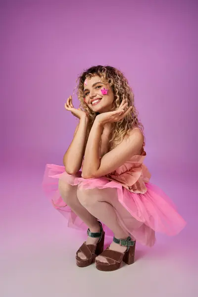 Lovely jolly woman in pink costume of tooth fairy with face stickers squatting raising hands to face — Stock Photo