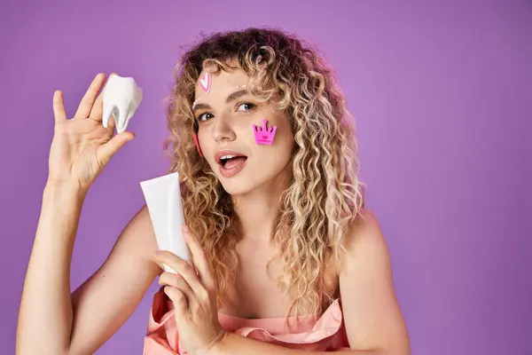 Lovely attractive woman with curly hair and face stickers holding baby tooth and tooth paste — Stock Photo