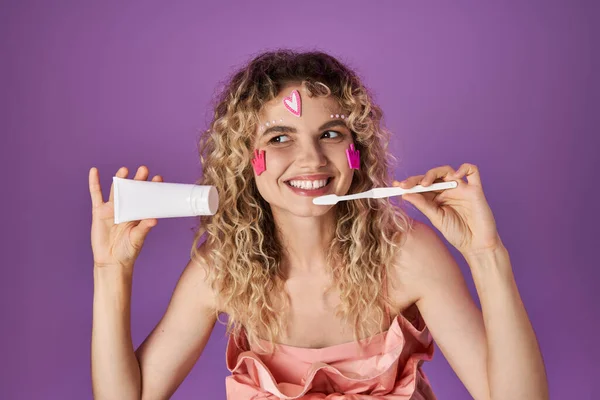 Fada de dente loira sorridente em traje rosa com adesivos faciais segurando escova de dentes e pasta dental — Fotografia de Stock