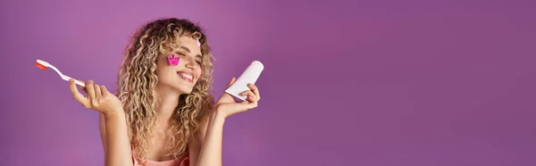 Attraktive, fröhliche Frau mit lockigem Haar und Gesichtsaufkleber mit Zahnbürste und Paste, Banner — Stockfoto