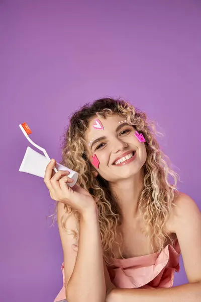 Retrato de mujer alegre con cepillo de dientes y pasta en las manos sonriendo y posando sobre fondo rosa - foto de stock