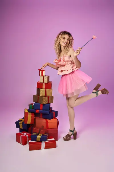 Mujer alegre en traje de hada diente de pie en una pierna al lado de un montón de regalos que sostienen varita mágica - foto de stock