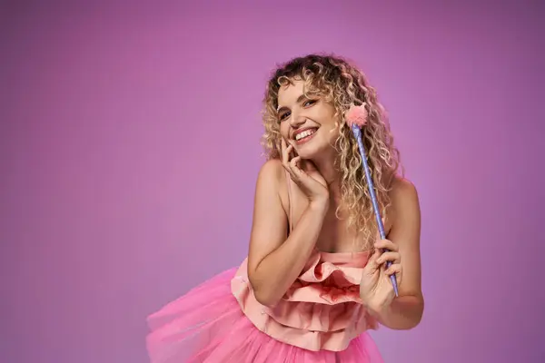 Linda fada do dente encaracolado em traje rosa vibrante segurando varinha mágica e sorrindo sinceramente para a câmera — Fotografia de Stock