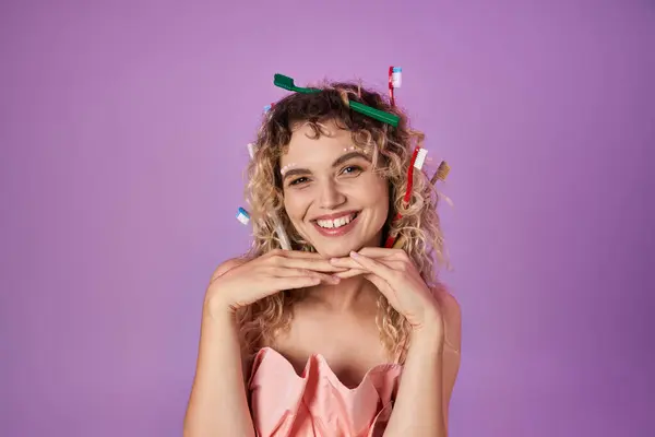 Бодрая зубная фея в розовом наряде и зубных щетках в кудрявых волосах позирует с руками под подбородком — стоковое фото